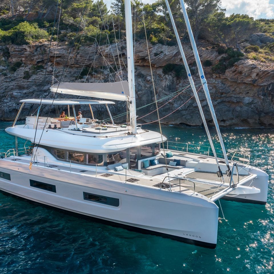 Lagoon 60 luxury sailing catamaran at anchor near rugged shoreline