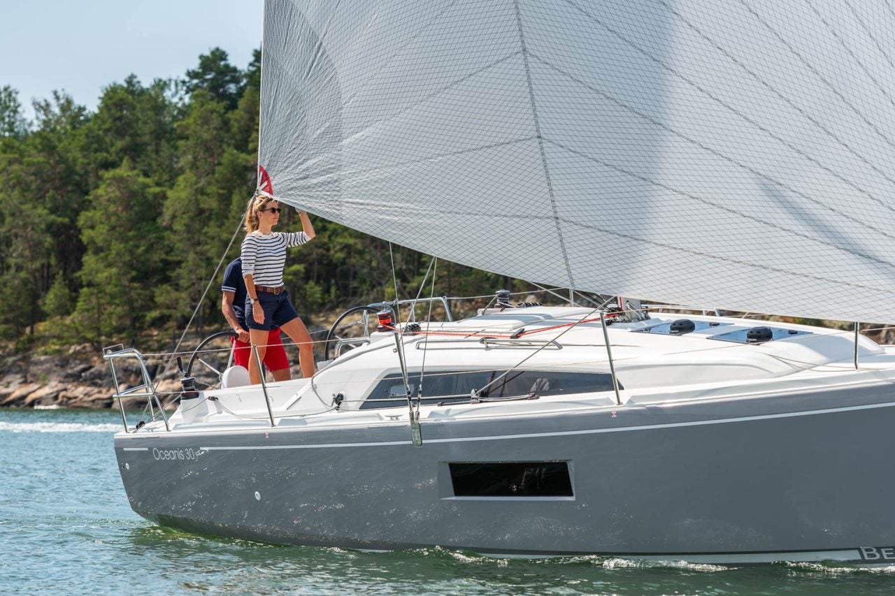 Closeup side view of Beneteau 30.1 monohull at sail with couple onboard