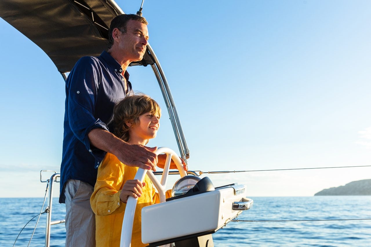 Man and son at helm of a Dufour model monohull sailboat