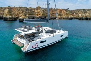 Fountaine Pajot Elba 45 sailing catamaran at anchor near cliffs